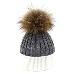 Détail du bonnet en tricot gris avec revers blanc et pompon en fourrure marron