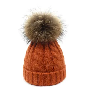 Detalle del tejido de trenzas de un gorro de invierno naranja con gran pompón de piel