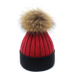Détail du bonnet en maille côtelée rouge et noir avec un pompon en fourrure moelleuse