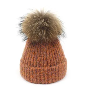 Warme gebreide dames muts voor de winter met grote pompon in de kleur burnt orange