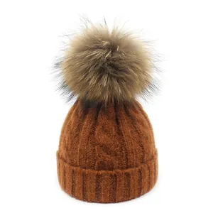 Detalle de gorro de punto color caramelo con patrón de trenzas y pompón de piel grande