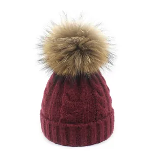 Detalle del gorro de punto trenzado burdeos con un pompón de piel sintética suave