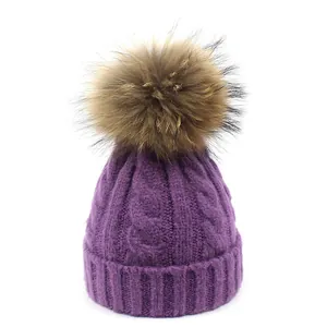 Detalle del gorro de punto violeta con trenzado grueso y un suave pompón de piel grande