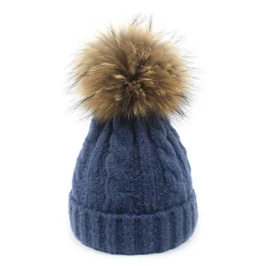 Detalle de gorro de punto trenzado azul oscuro con pompón grande de piel marrón suave