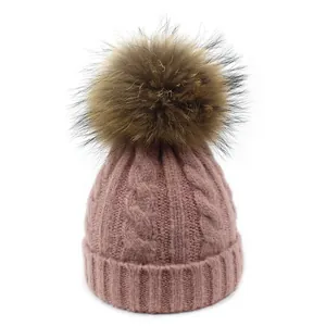 Primer plano de gorro de punto trenzado con pompón de piel grande y borde doblado