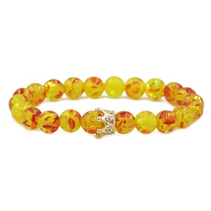 Detail of amber resin beads with a golden CZ crown charm on an elastic bracelet