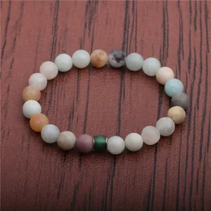 Buntes Naturstein-Perlenarmband mit grünem Zylinder-Anhänger auf Holzhintergrund