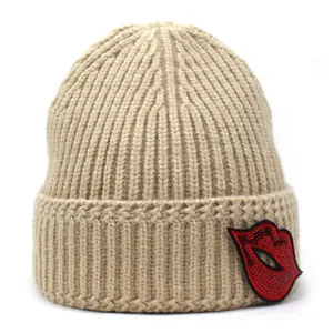 Makroansicht der beigen Strickmütze mit Pailletten-Lippen-Aufnäher am umgeschlagenen Rand
