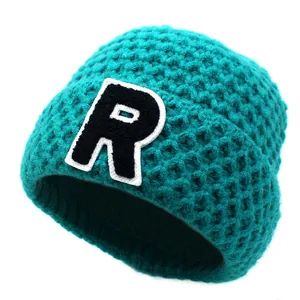 Close-up of turquoise knit beanie featuring a black letter R patch and honeycomb texture