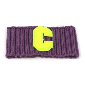 Detail eines lila gerippten Strickstirnbands mit neongelbem Buchstaben C Patch