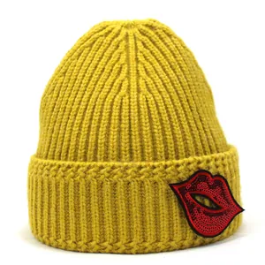 Detail der gelben Strickmütze mit rotem Pailletten-Lippen-Stickaufnäher am Umschlag