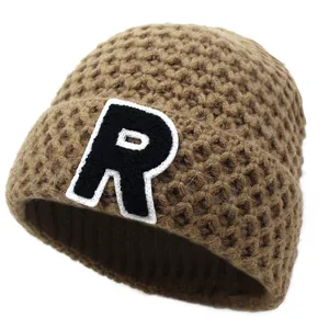 Close-up of thick knit beanie in brown featuring a white R letter patch and texture