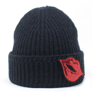 Detail der schwarzen Strickmütze mit rotem Lippen-Pailletten-Patch am umgeschlagenen Rand