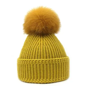Detail van gele ribgebreide muts met een grote bijpassende pompon van imitatiebont