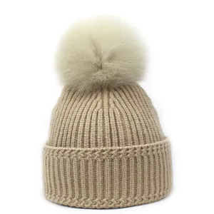 Detail van beige gebreide muts met imitatiebont pompon en brede omgeslagen rand voor dames