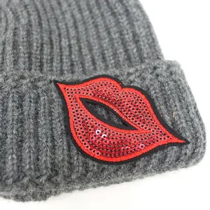 Graue Strickmütze mit roten Pailletten-Lippen und Rippenmuster auf weißem Grund