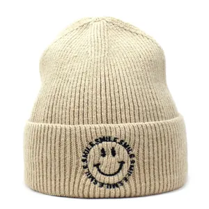 Detailed view of beige ribbed beanie featuring black smile embroidery and text