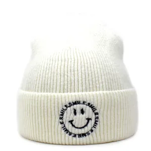 Detail of smile face embroidery and 'SMILE' text on cream knitted beanie hat