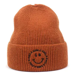 Detailed texture of caramel knit beanie featuring black smile face embroidery on the cuff
