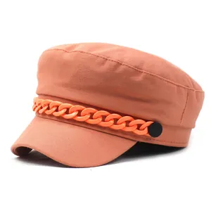 Detail of a burnt orange flat top military cap with a chunky chain and side buttons
