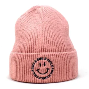 Close-up of pink ribbed knit beanie featuring black smile embroidery on the folded cuff