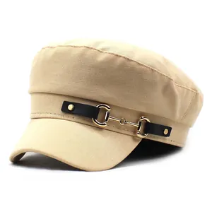 Detail of beige baker boy hat featuring a black leather strap and golden horsebit buckle
