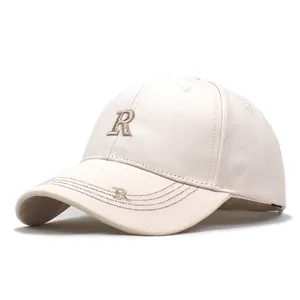 Detalle de bordado R dorado en gorra de béisbol beige con costuras de alta calidad y visera