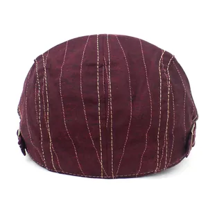 Burgundy cotton flat cap with yellow stitching and metal side buckles on white background