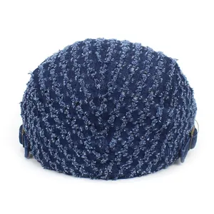 Detail of blue denim newsboy cap featuring distressed fringe and vintage metal buckles