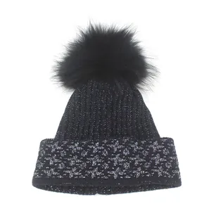 Close-up of black knitted beanie featuring silver jacquard patterns and a fluffy faux fur pompom