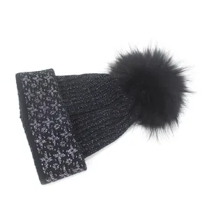 Close-up of black ribbed knit beanie with silver glitter pattern and fluffy faux fur pompom