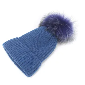 Détail du bonnet en maille bleu marine avec un pompon violet duveteux et épais