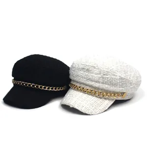Detail of tweed newsboy caps in black and white with decorative gold metal chains