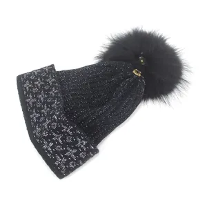 Close-up of black knit beanie with silver thread and fluffy faux fur pom-pom detail