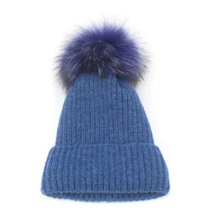 Détail du bonnet en maille bleu avec un pompon moelleux en fausse fourrure violette