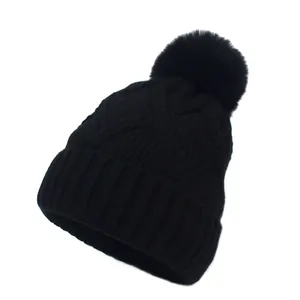 Cable knit winter beanie for women in black featuring a fluffy faux fur pompom top