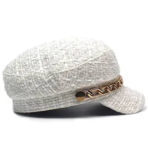 Detail of white tweed newsboy hat featuring textured fabric and golden chain link accessory
