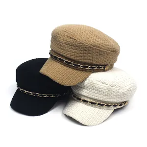 Detail view of tweed newsboy caps in black, khaki, and white with decorative gold chains