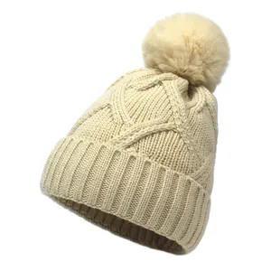 Beige chunky cable knit winter beanie with a large faux fur pom and ribbed cuff