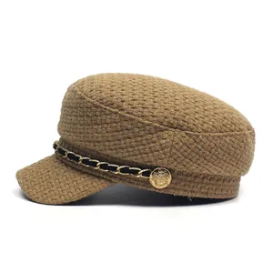 Close-up of brown textured plaid newsboy hat with gold chain and heraldic button detail