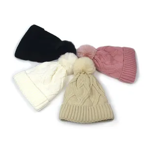 Flat lay of cable knit beanies in four colors with fluffy faux fur pompoms