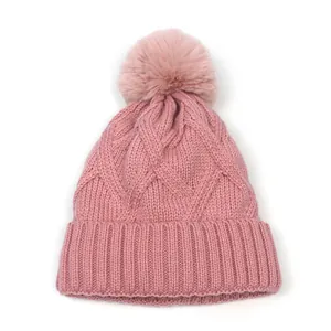 Close-up of pink knit beanie with intricate cable texture and soft faux fur pom-pom