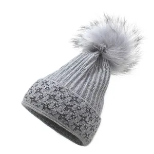 Close-up of grey knit beanie with fluffy faux fur pompom and silver glitter star details