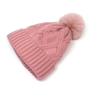 Close-up of pink cable knit beanie featuring a soft faux fur pom-pom and thick texture
