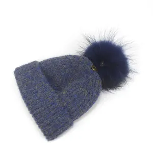 Detailed view of the blue knitted beanie featuring a textured weave and large fluffy pompom