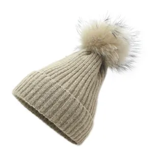 Détail de la texture en maille côtelée et du pompon en fourrure sur un bonnet couleur avoine