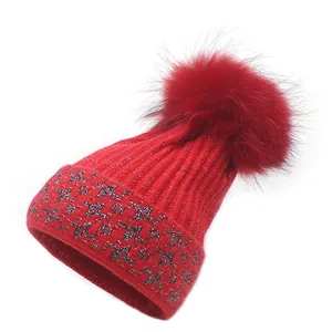 Detailed knit texture of red beanie with silver star sequins and fluffy faux fur pompom