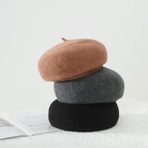 Close-up of caramel, dark grey, and black wool berets stacked on a minimalist background