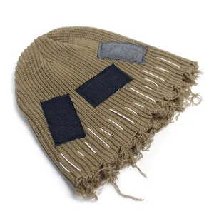 Detail of khaki distressed knit beanie featuring denim patches and raw frayed edges