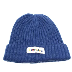 Dettaglio della maglia e patch colorata LibreJeu su un berretto in maglia blu scuro